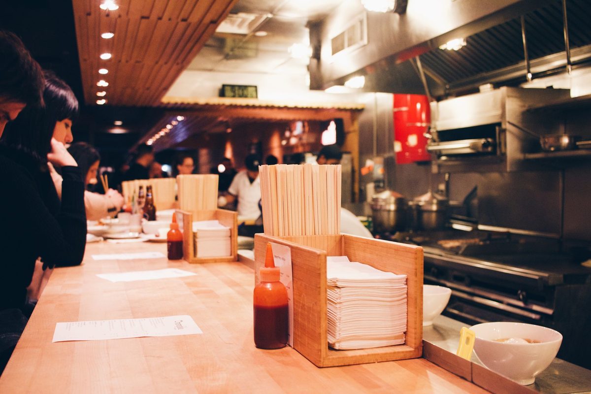 麵館店面情境示意：暖色燈光的用餐吧檯與開放式廚房